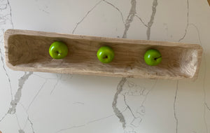 A wooden trug filled with three green apples on a marble countertop.