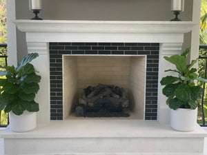 Two fiddle-leaf figs in matte white ceramic pots next to a fireplace.