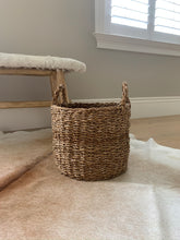 Load image into Gallery viewer, A brown woven basket in front of a bench.
