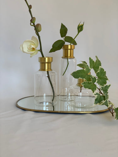 Bud vases on a mirrored tray with fake buds and leaves inside them.