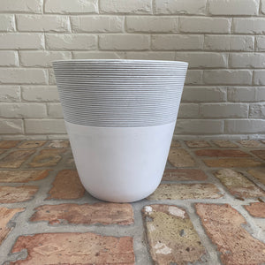 A white and gray-striped pot on a brick patio.