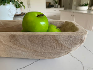 A close-up of a wooden trug filled with green apples on a marble countertop.